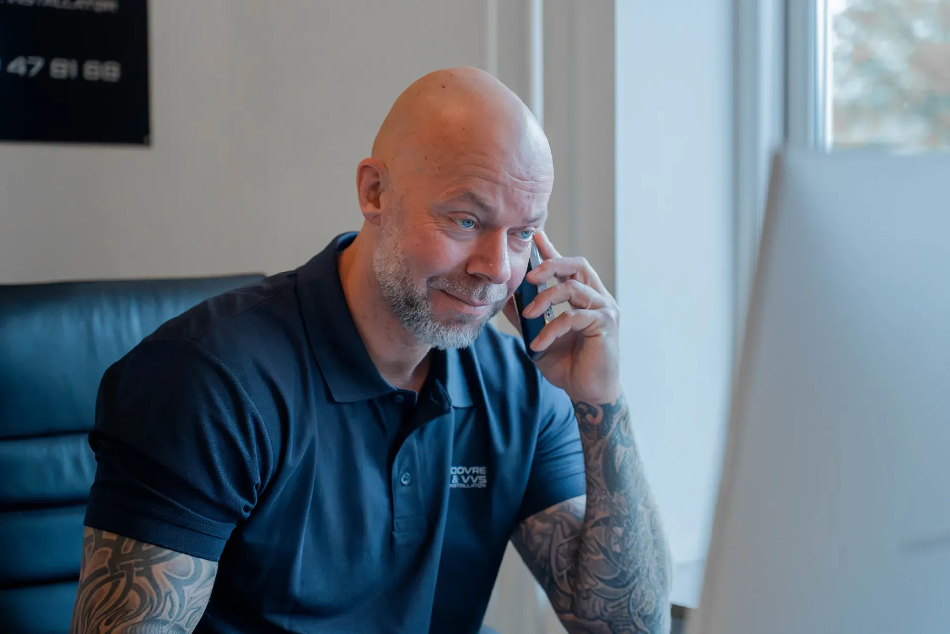 Mandlig VVS-arbejder taler i telefon, iført blå uniform med logo.