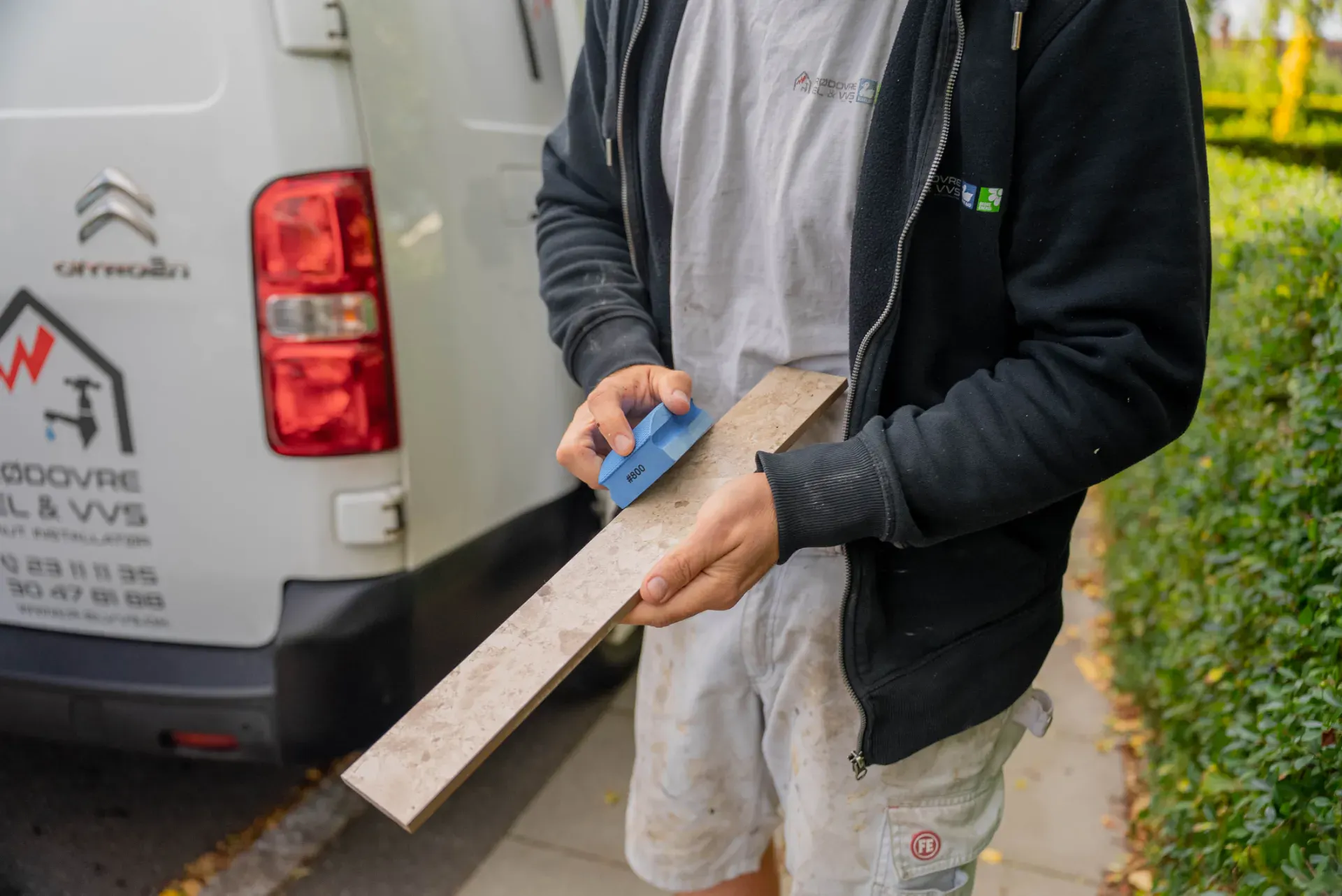 Mand arbejder med træmateriale foran Rødovre El & VVS bil.